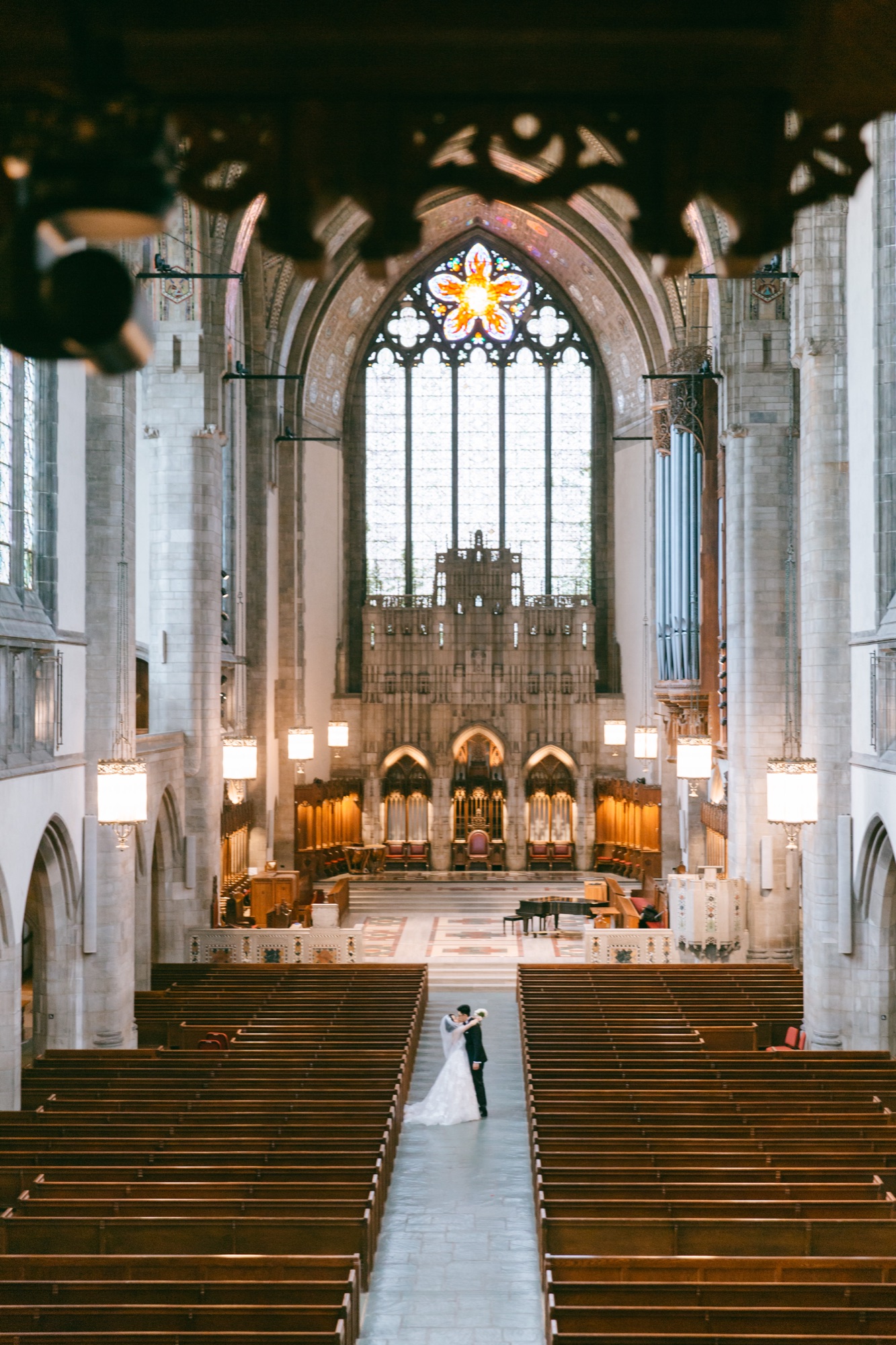 A wide church interior with a couple centered in the aisle