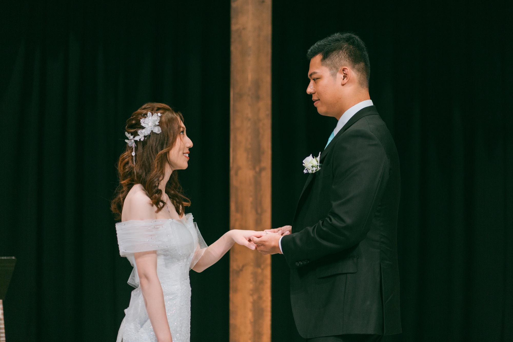 A couple exchanging rings against a dark background