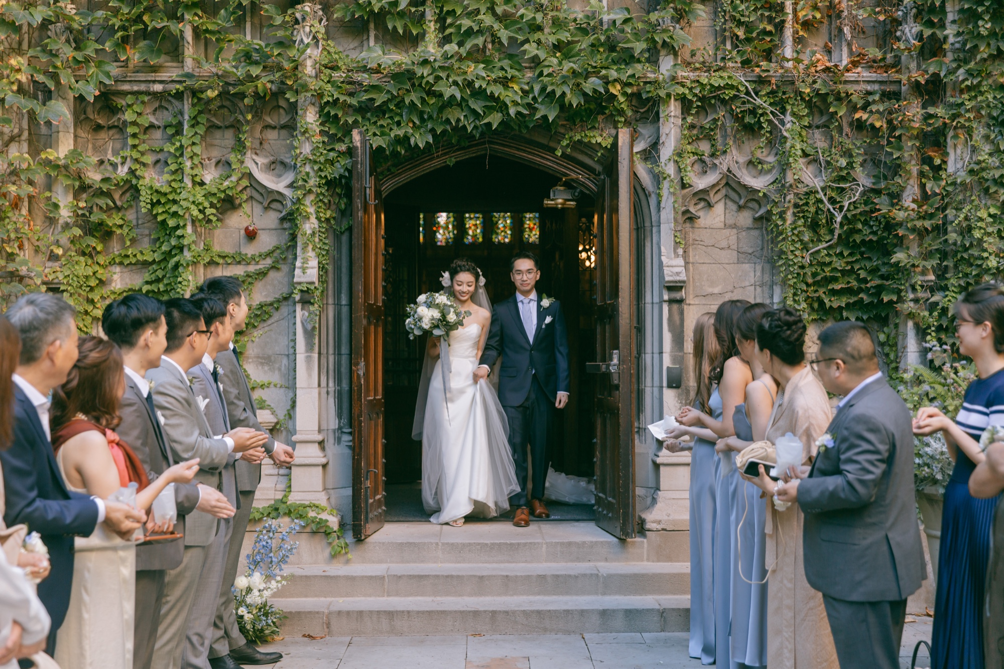 Newlyweds exiting an ivy-covered church doorway between guests