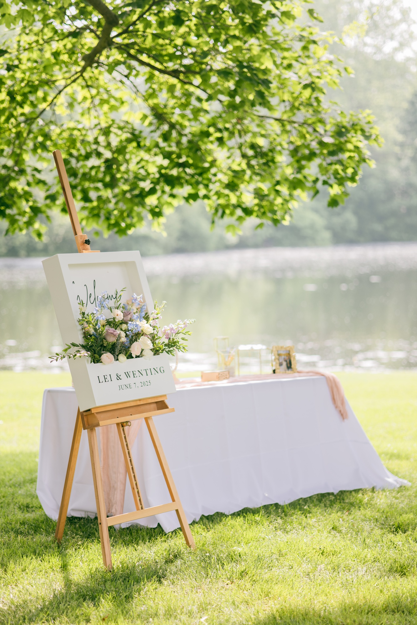 A floral welcome sign and reception table beside a lake