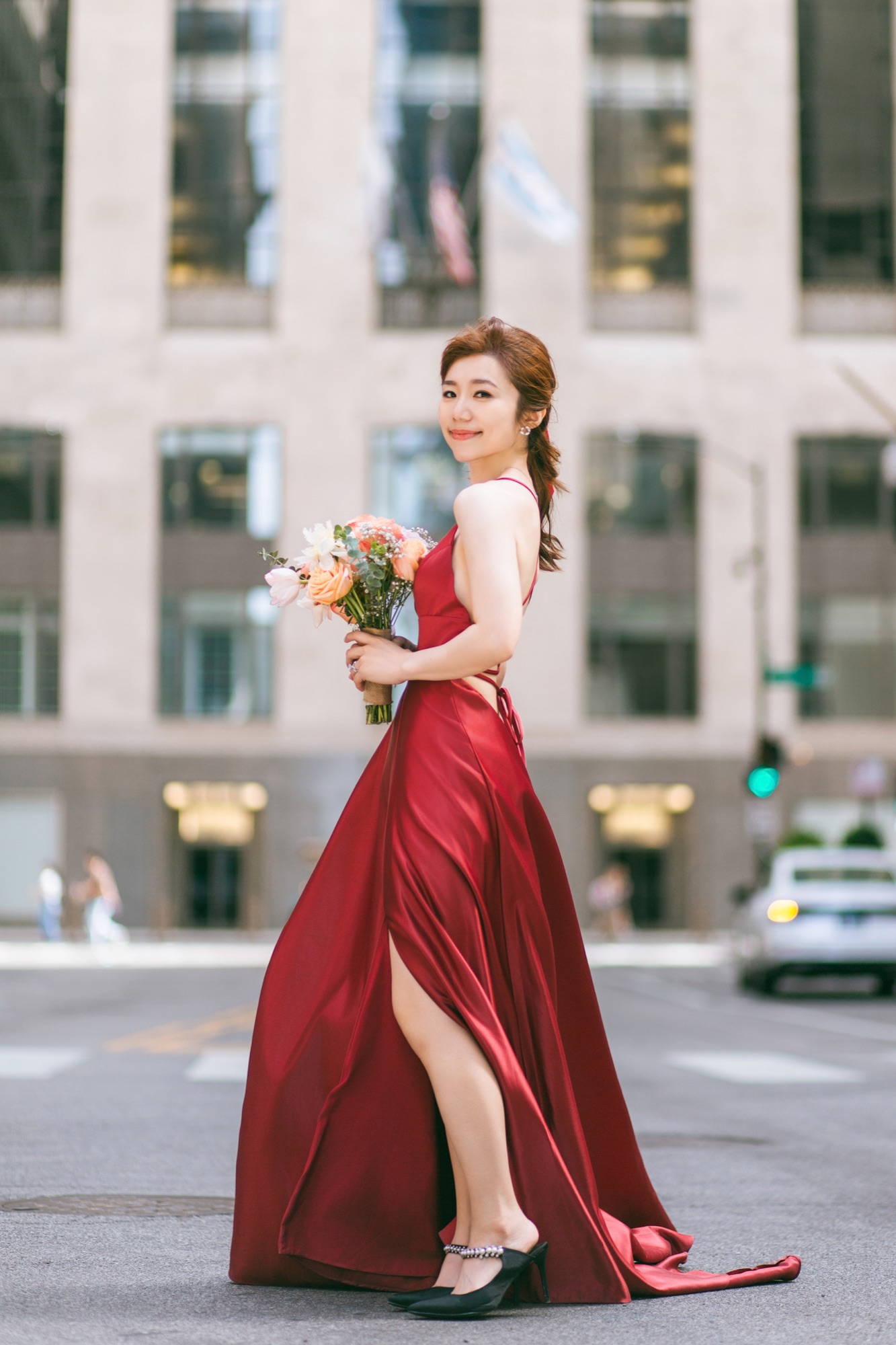 A bride in a red gown holding a bouquet on a city street