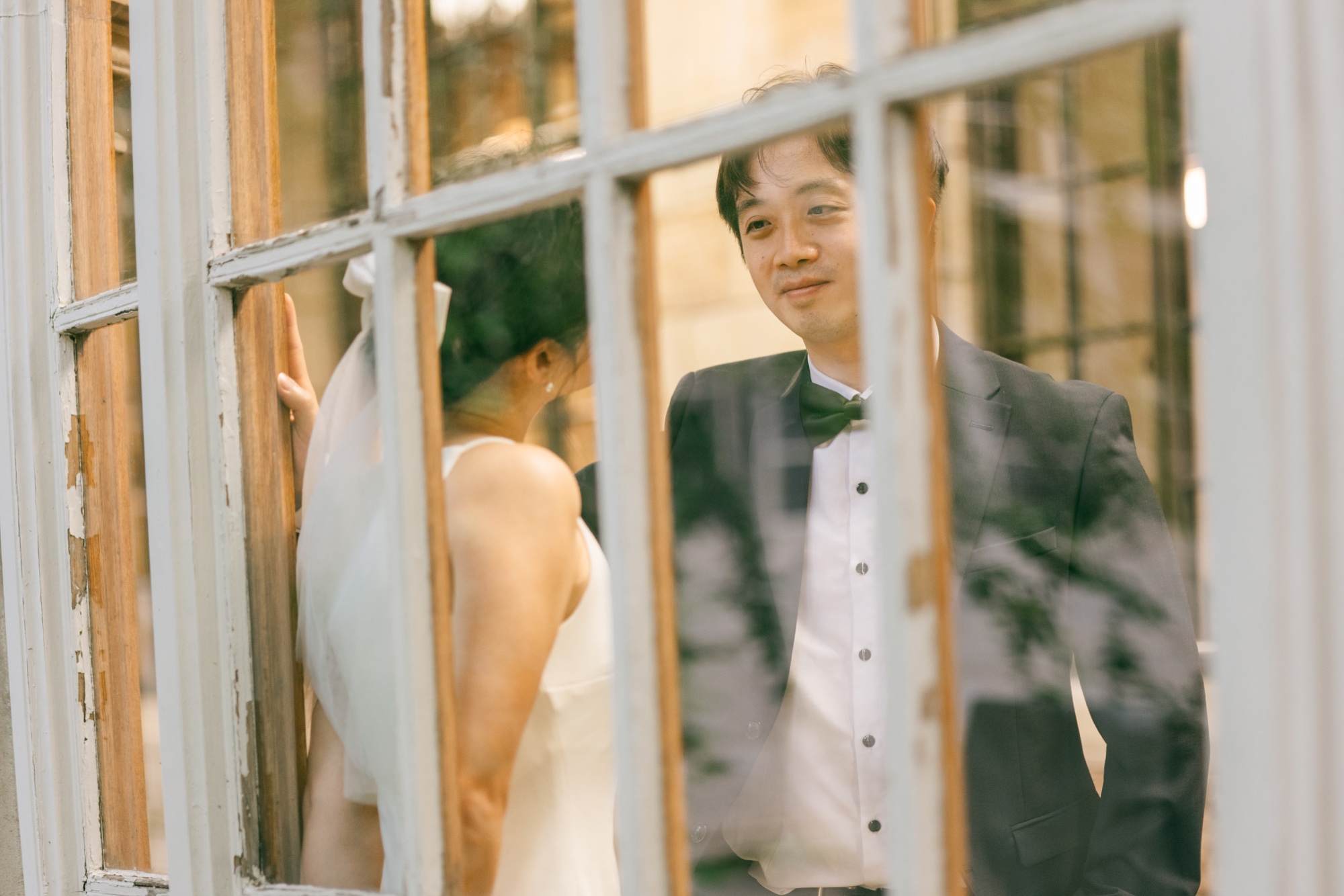 A bride and groom seen through window panes in warm light