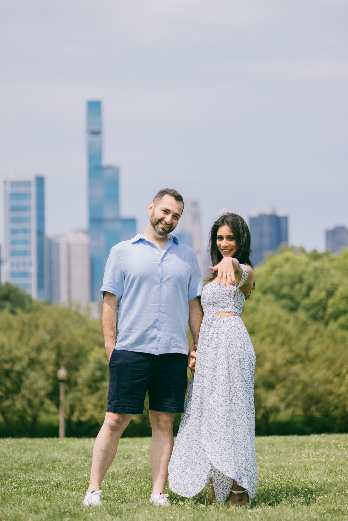 A couple showing an engagement ring with the Chicago skyline behind them